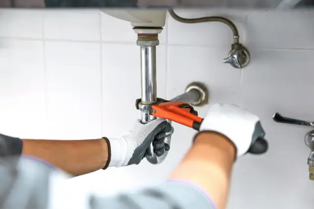 Plumber fixing a water pipe with a wrench in a residential bathroom